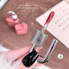 Lip gloss with a brush head held by a hand on a wooden surface.