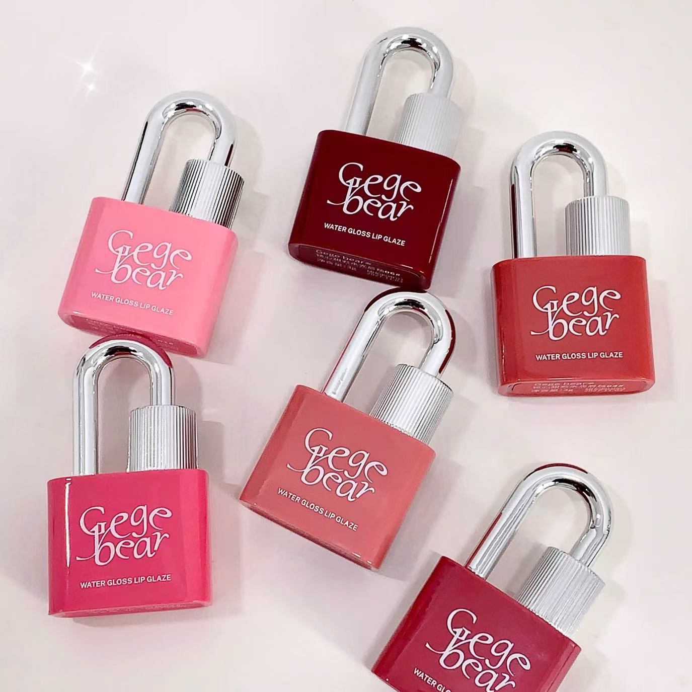 Red and pink 'Geg bear' lip glosses with lock designs on a light pink background