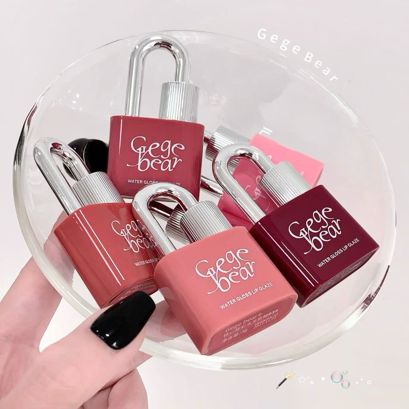 Lock-shaped lip glosses with 'Gee Bear' branding on a clear stand.