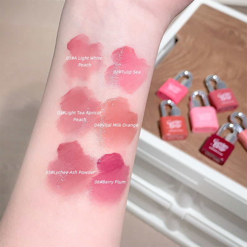 Lipstick swatches on a wrist with labeled colors, next to small pink lock-shaped items.